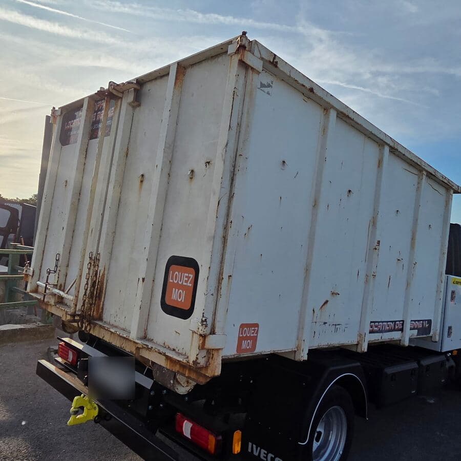 Camion vu de l’arrière, chargé d’une benne blanche portant l’autocollant « Louez-moi », plaque floutée