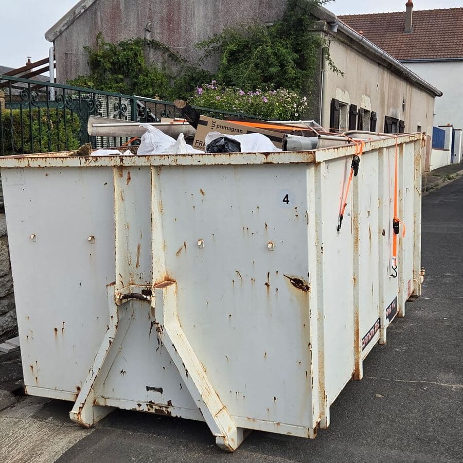 Benne blanche numérotée 4, remplie et sanglée, posée sur la chaussée devant une maison